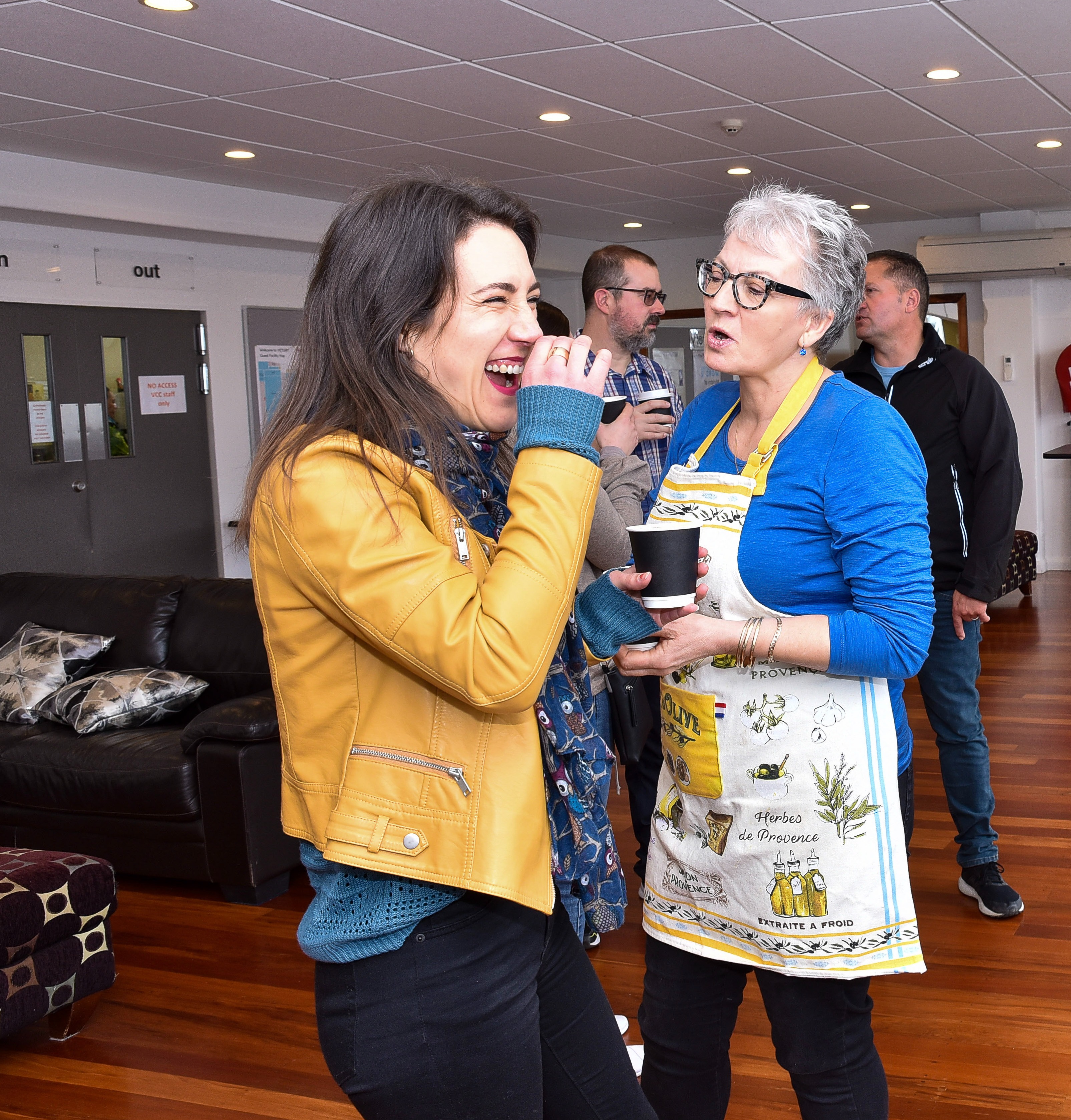 Women in mustard jacket laughing to joke being told