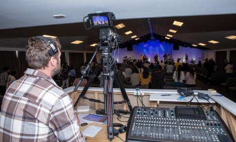 Man taking video of sermon from booth.